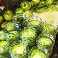 several jars filled with green liquid sitting on top of a counter next to tomatoes and peppers