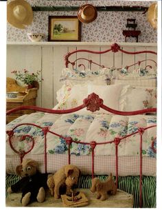 two teddy bears sitting on a bed in a room with floral wallpaper and red iron bedspread