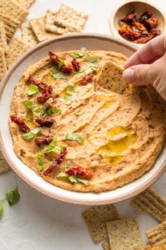 a hand dipping some crackers into a bowl of hummus and tortilla chips