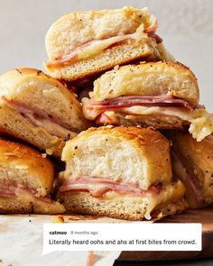 a pile of ham sandwiches sitting on top of a wooden cutting board