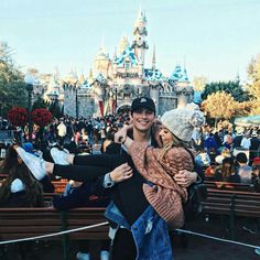 two people standing in front of a castle with their arms around each other and kissing