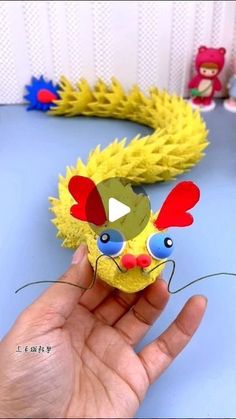 a hand holding a yellow toy with red, blue and green decorations on it's face