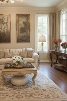 a living room filled with furniture and flowers on top of a coffee table in front of two windows