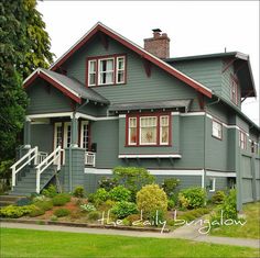 a gray house with red trim and windows on the front porch is surrounded by greenery