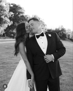 a man in a tuxedo kissing a woman in a white dress on the grass