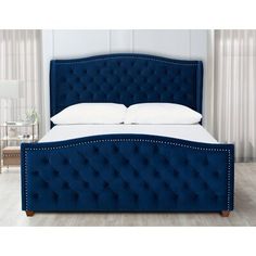 a blue upholstered bed frame with white pillows and buttons on the headboard