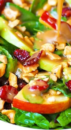 a salad with apples, cranberries, walnuts and dressing being drizzled on top