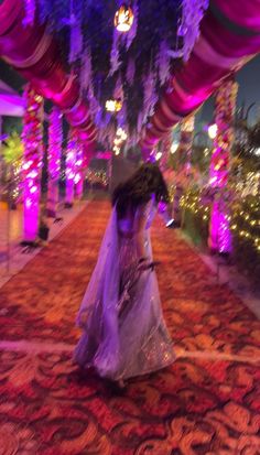 a woman in a white dress is walking down a red carpeted walkway with lights on it