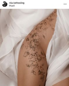 a woman laying on top of a bed covered in white sheets with tattoos on her legs