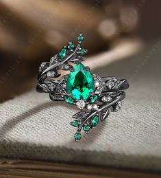 a ring with green stones and leaves on it sitting on top of a cloth covered table