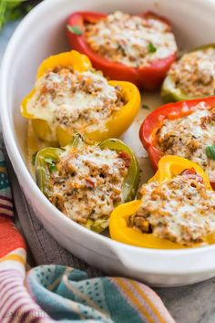 stuffed bell peppers in a white casserole dish with cheese and seasoning on top