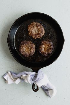 three hamburger patties are cooking in a cast iron skillet on a white surface