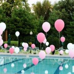 pink and white balloons floating in the air near a swimming pool