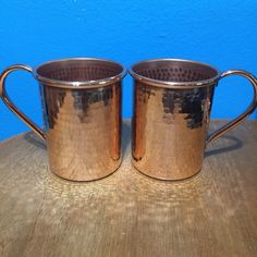 two shiny metal mugs sitting on top of a wooden table next to each other