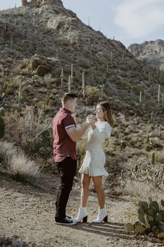 a man and woman standing in the desert drinking wine