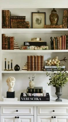 a bookshelf filled with lots of books next to a vase and busturine