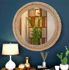 there is a mirror on the wall above a table with two lamps and a potted plant