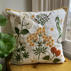 an embroidered pillow on a chair next to a potted plant in front of a window