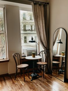 a table and chairs in front of a window with a large mirror on the wall