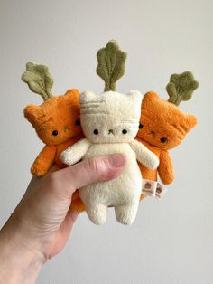 three stuffed animals are held in the palm of a person's hand, one is orange and the other is white