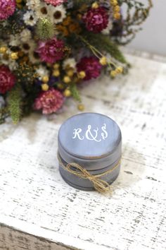 a small round box with the initials on it sitting on a table next to flowers