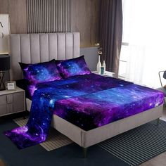 a bed room with a neatly made bed covered in purple and blue galaxy comforters