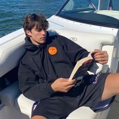 a young man sitting on the back of a boat reading a paper while wearing shorts