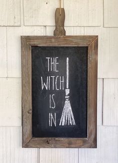 a chalkboard with the words the witch is in written on it hanging from a hook