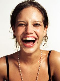 a woman laughing while wearing a necklace with pearls on it's neck and teeth