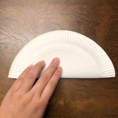 a person's hand on top of a paper plate that is sitting on a wooden table