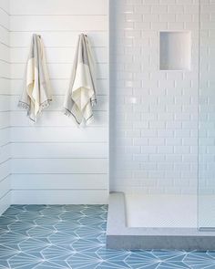 two towels are hanging on the wall next to a walk in shower with glass doors