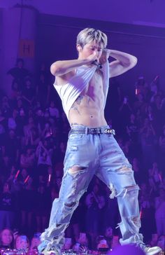 a man in ripped jeans on stage with his hands behind his head