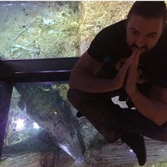 a man sitting on top of a glass floor in front of a fish tank with his hands together