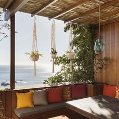 an outdoor seating area with hanging planters and potted plants on the balcony overlooking the ocean