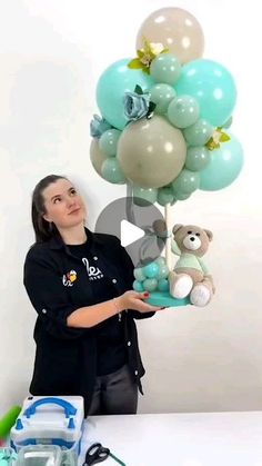 a woman holding a bunch of balloons in front of a teddy bear and balloon tree