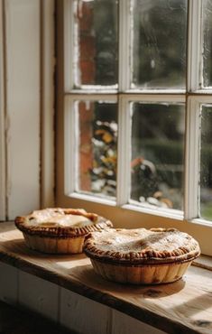 two pies sitting on a window sill in front of a large pane of windows