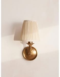 a gold wall light with a white shade on the lamp is shown against a white wall