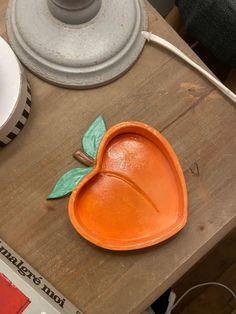 an orange heart shaped bowl sitting on top of a wooden table next to a lamp