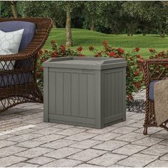 two wicker chairs and an outdoor storage box on a patio with flowers in the background