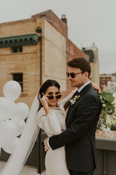 a bride and groom pose for a photo on the roof of their wedding venue with balloons in the background