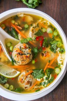 a bowl of soup with meatballs and veggies on the side next to a spoon