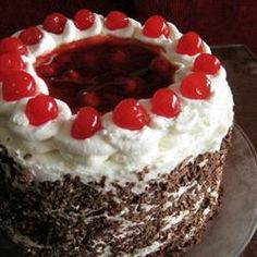 a cake with white frosting and red cherries on top is sitting on a plate