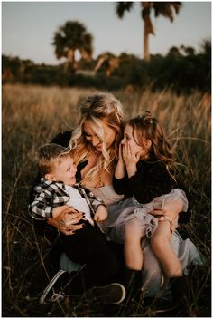 a woman and two children are sitting in the tall grass with palm trees behind them