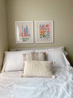 two framed pictures hang on the wall above a bed with white linens and pillows