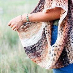 a woman wearing a crocheted shawl standing in a field with her hands on her hip