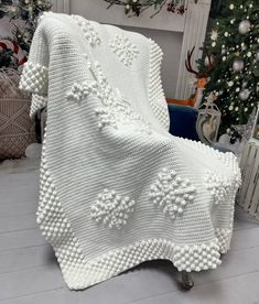 a white crocheted blanket sitting on top of a wooden floor next to a christmas tree