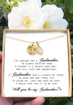 a hand holding a gold necklace with a poem in the middle and a white flower behind it