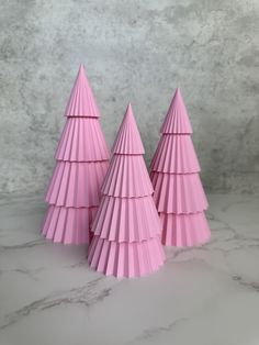 three pink paper christmas trees sitting on top of a marble countertop next to each other