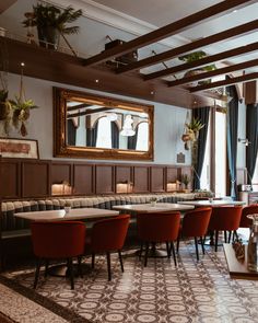 a restaurant with long tables and red chairs in front of a large mirror on the wall