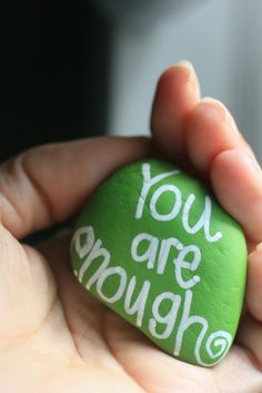 a person holding a green rock with the words you are enough written on it in white